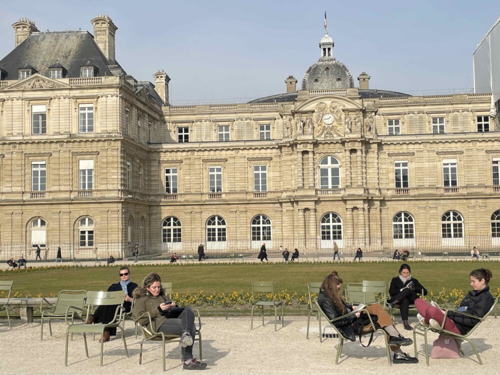 paris-france-luxembourg-park-people-chairs-sitting-in-front-of-elegant-architecture